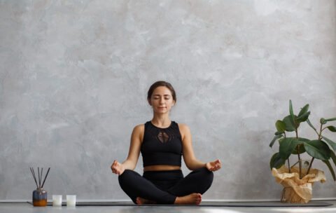 Portrait of sporty young woman doing exercises on yoga lesson at home. Beautiful girl practicing easy yoga pose, sukhasana. Yoga postures,meditation,relaxation,stress management, wellbeing and health