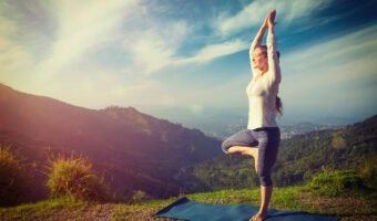 Woman in yoga asana Vrikshasana tree pose in mountains outdoors