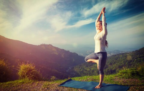 Woman in yoga asana Vrikshasana tree pose in mountains outdoors