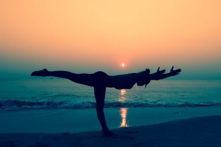 young woman practicing yoga on the beach at sunrise